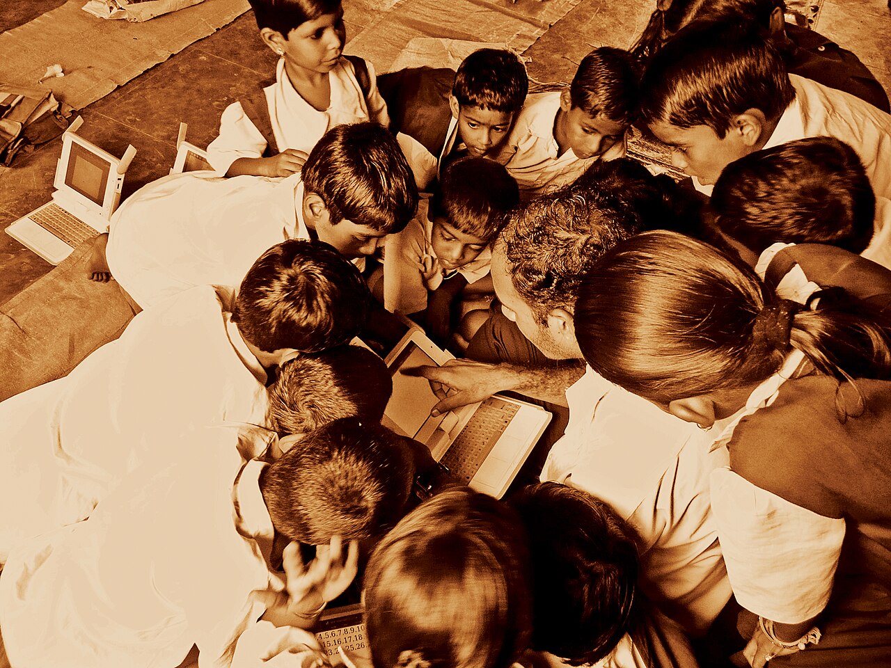 A group of schoolchildren in India gathered around small laptops