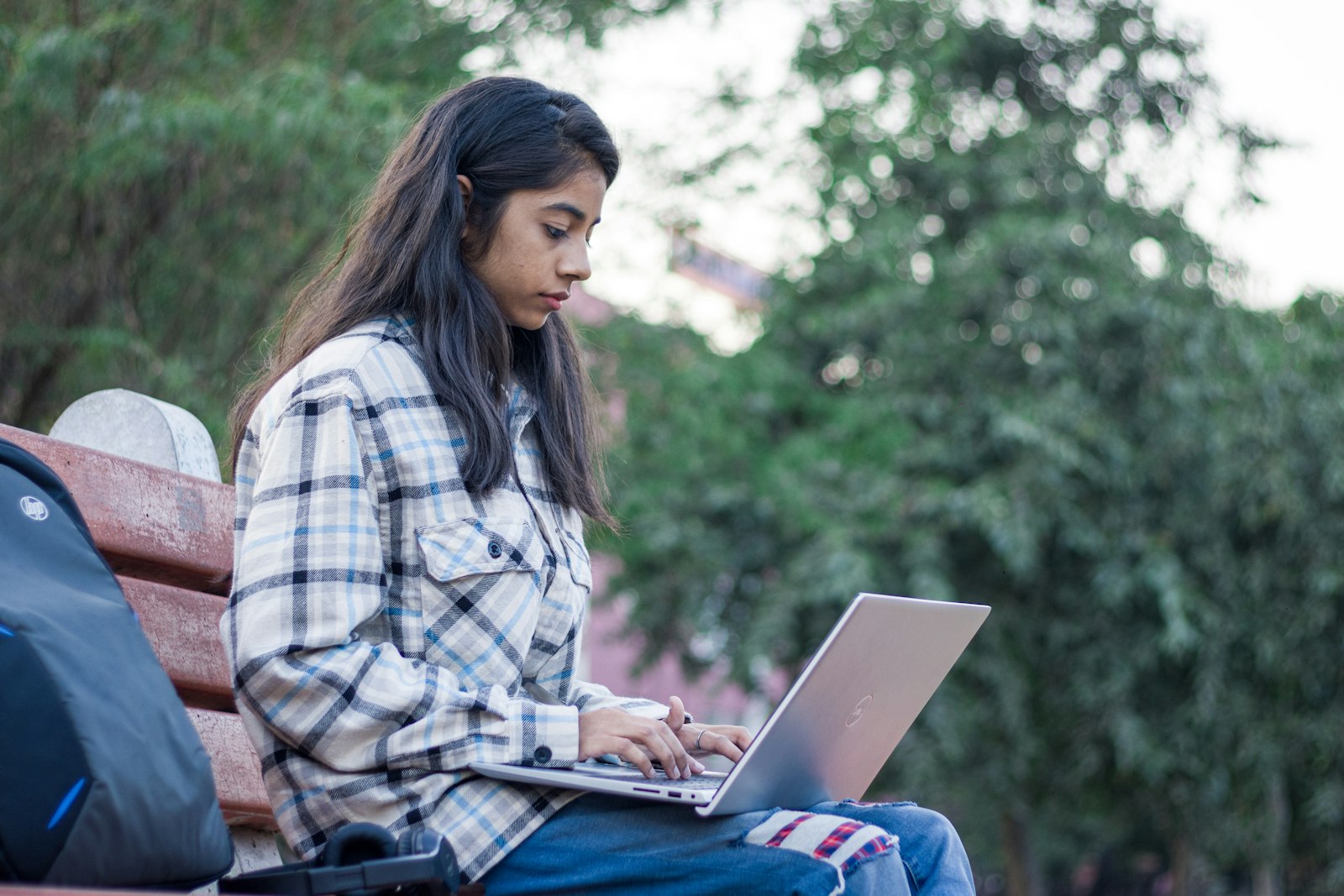 A teenager sitting on a bench using a laptop.