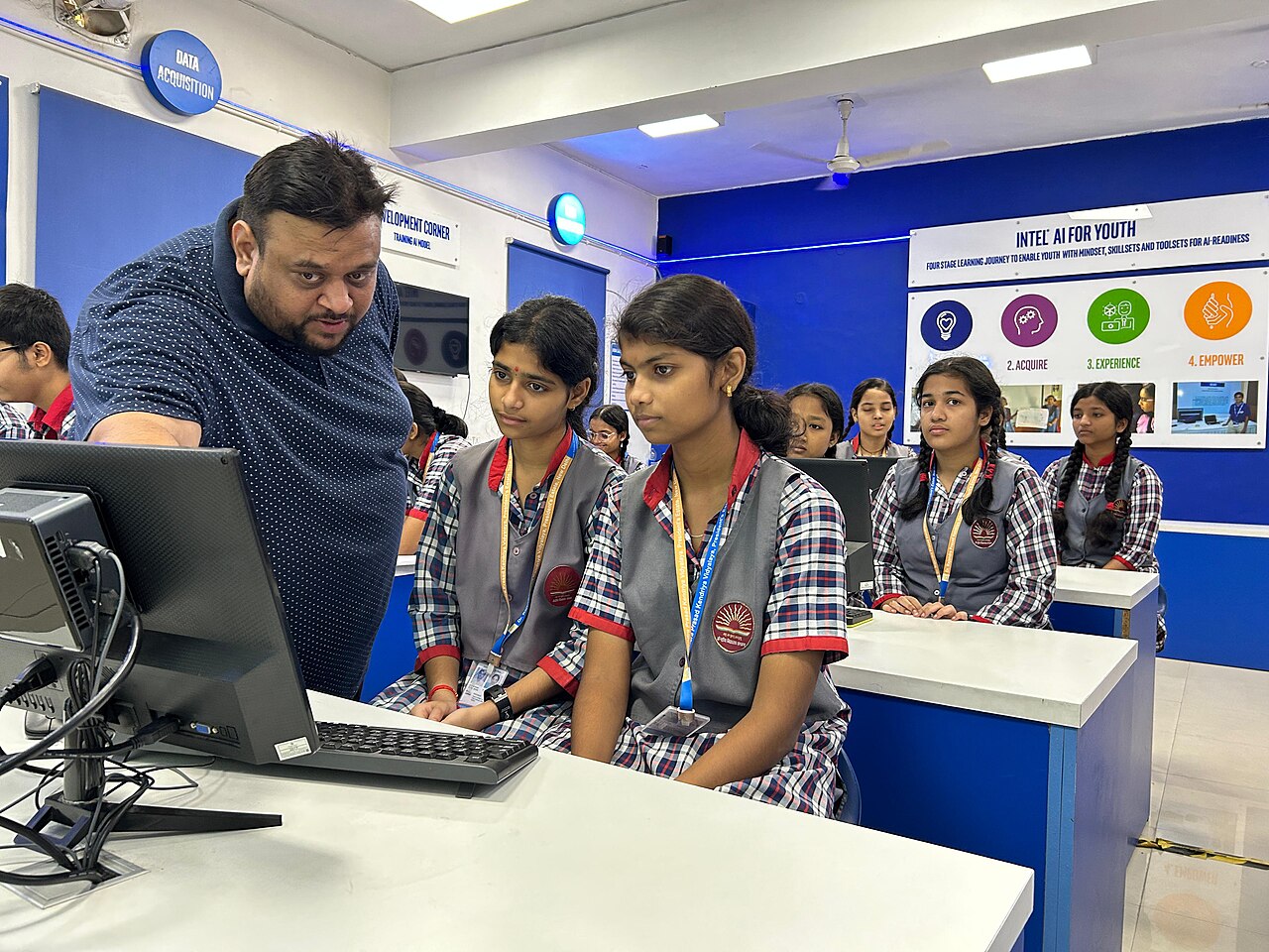 A computer science teacher guiding students in the AI lab of a Kendriya Vidyalaya