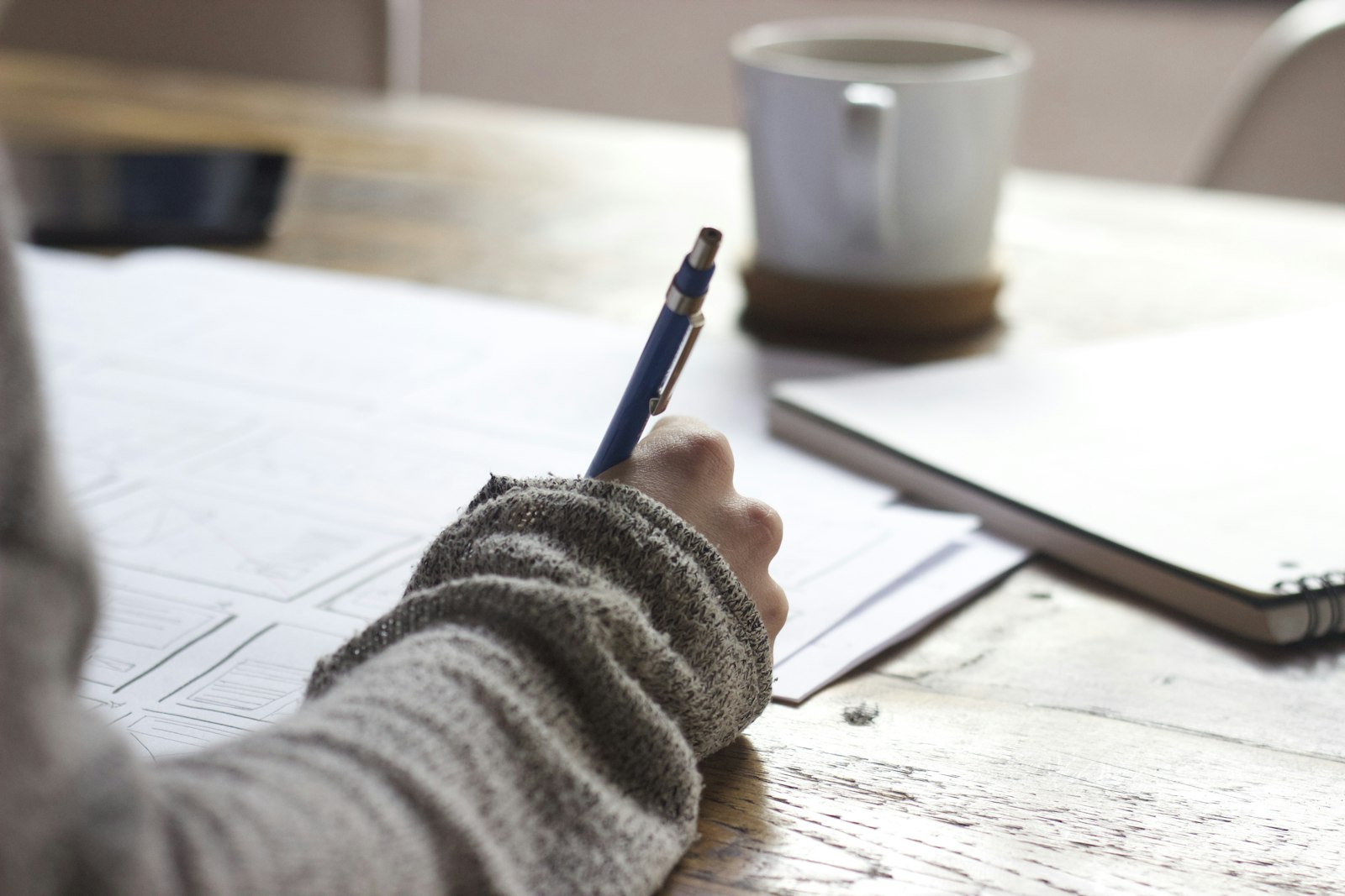 A student writing on paper at a wooden table, checking details