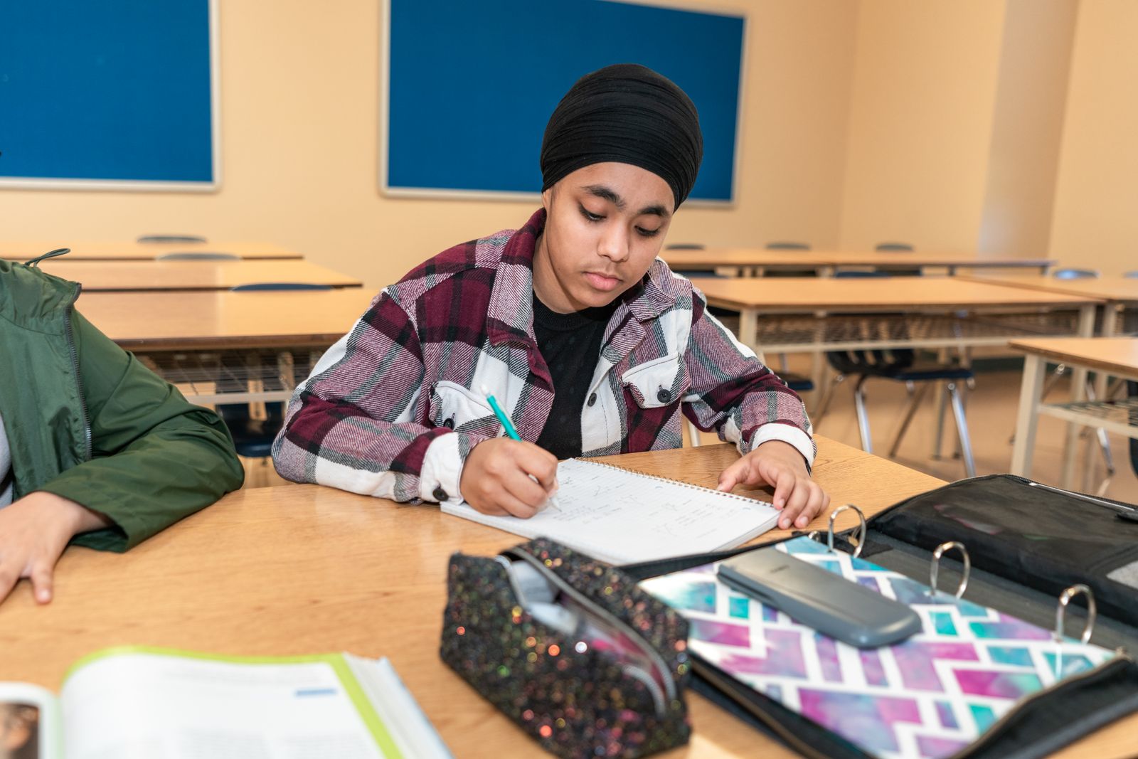 Teenage student writing an answer at a classroom desk during practice.
