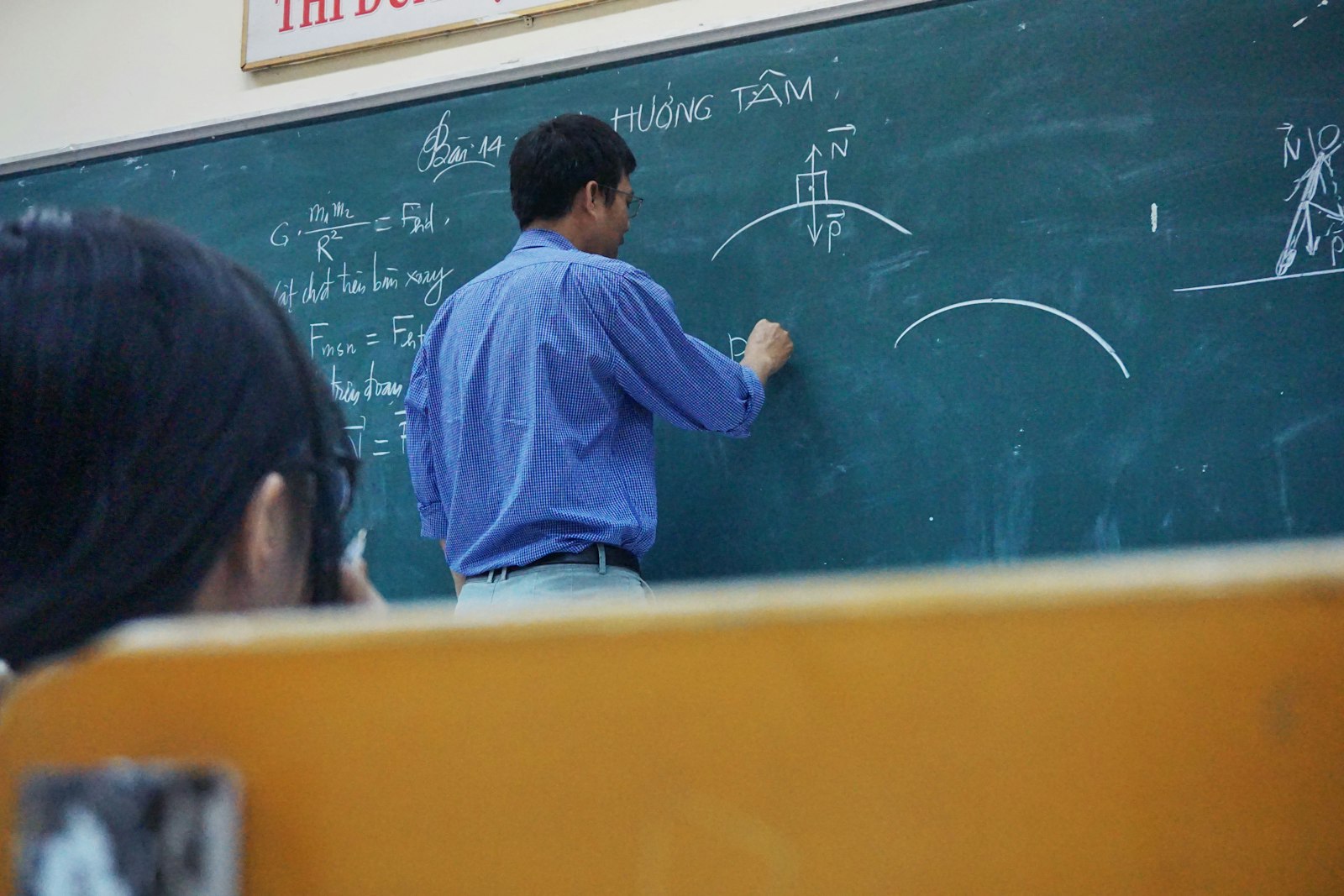 A teacher writing physics equations on a green chalkboard