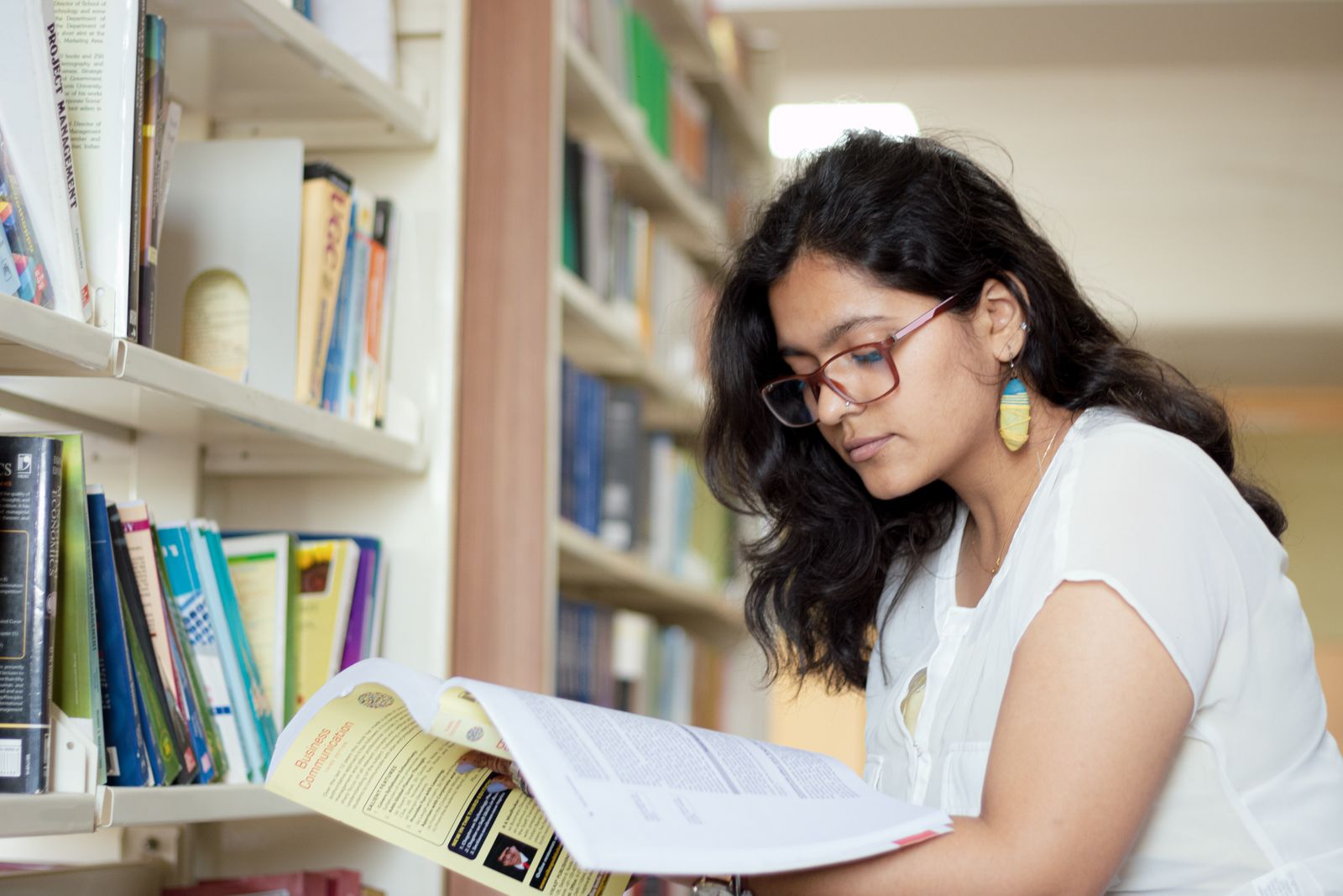 Young Indian student reading a book between library shelves