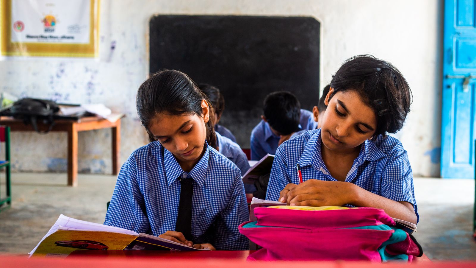 Two Indian schoolgirls in uniform concentrating on written work at a desk.