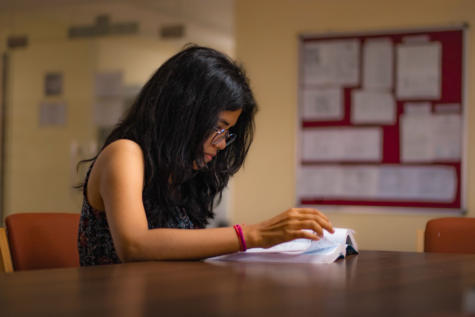Student reading a textbook at a library desk while revising for board exams.