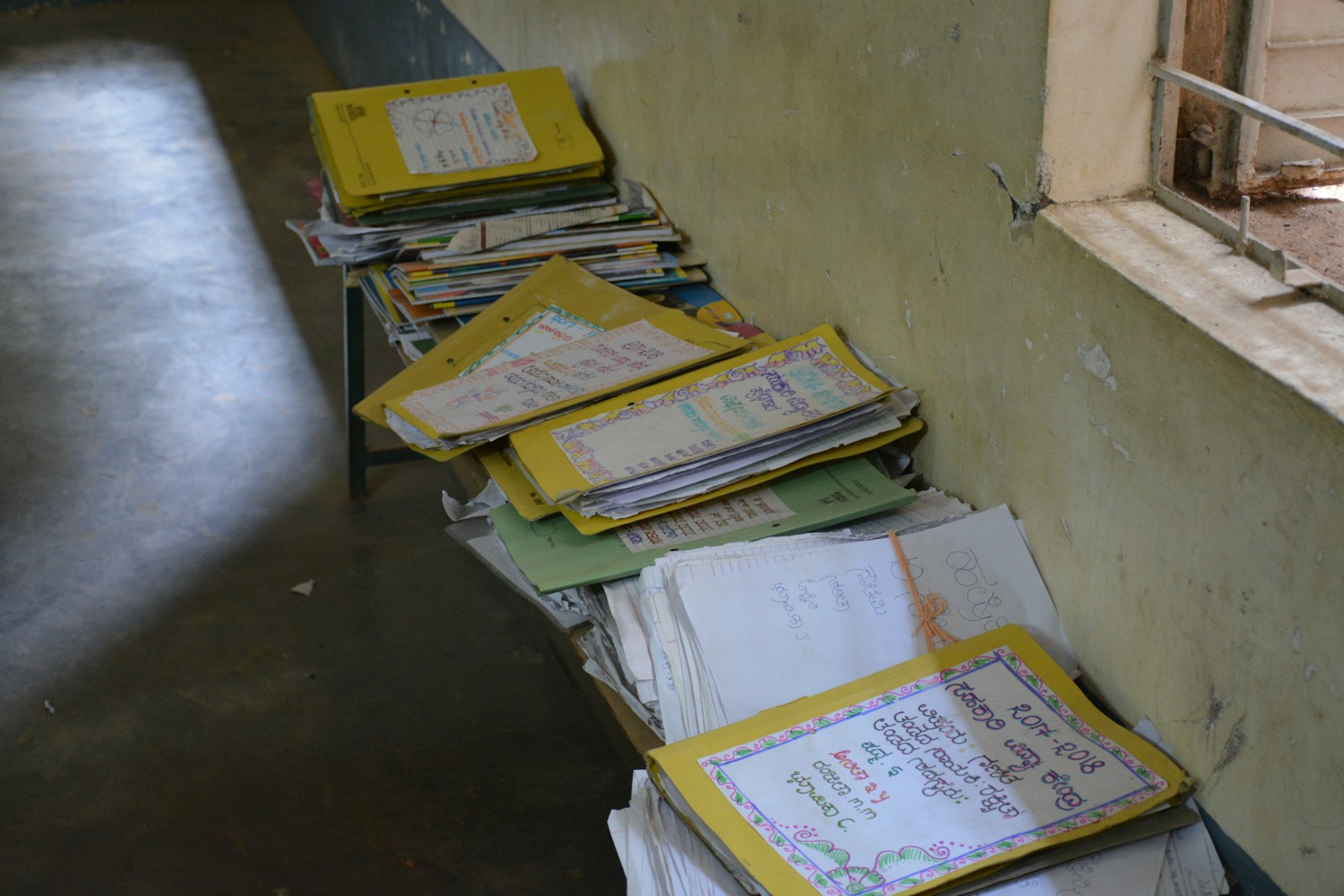Stacks of student workbooks and project files in a government school corridor