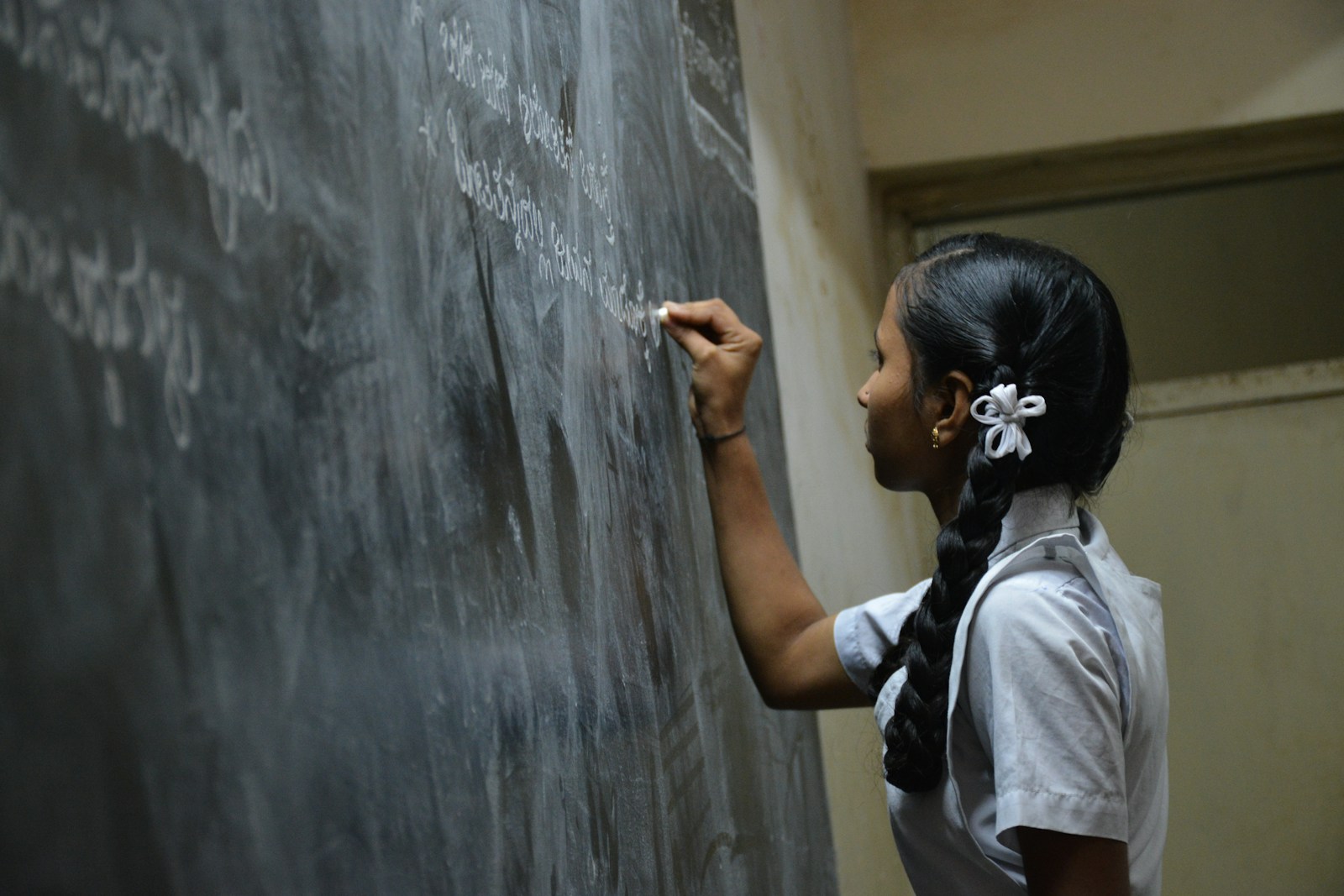 A school student in uniform writing an answer on the classroom chalkboard