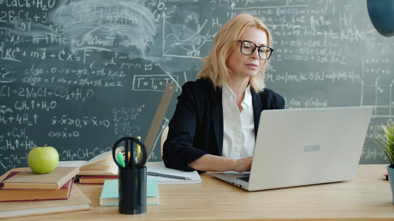 Teacher working on a laptop in front of a chalkboard