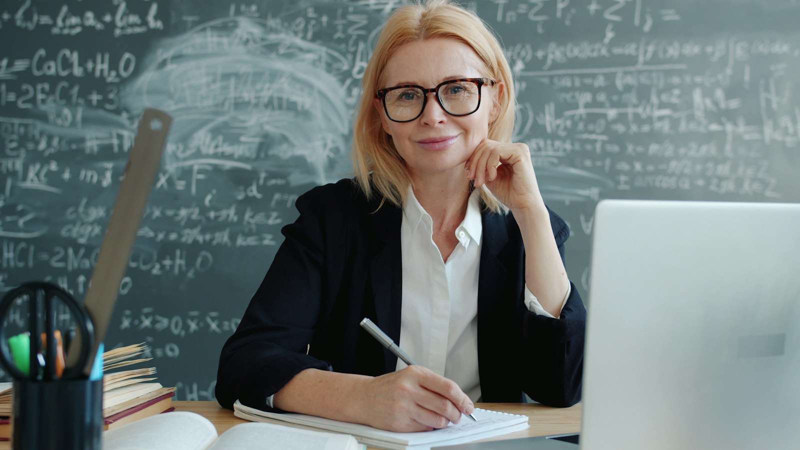 Teacher smiling at her classroom desk with a laptop