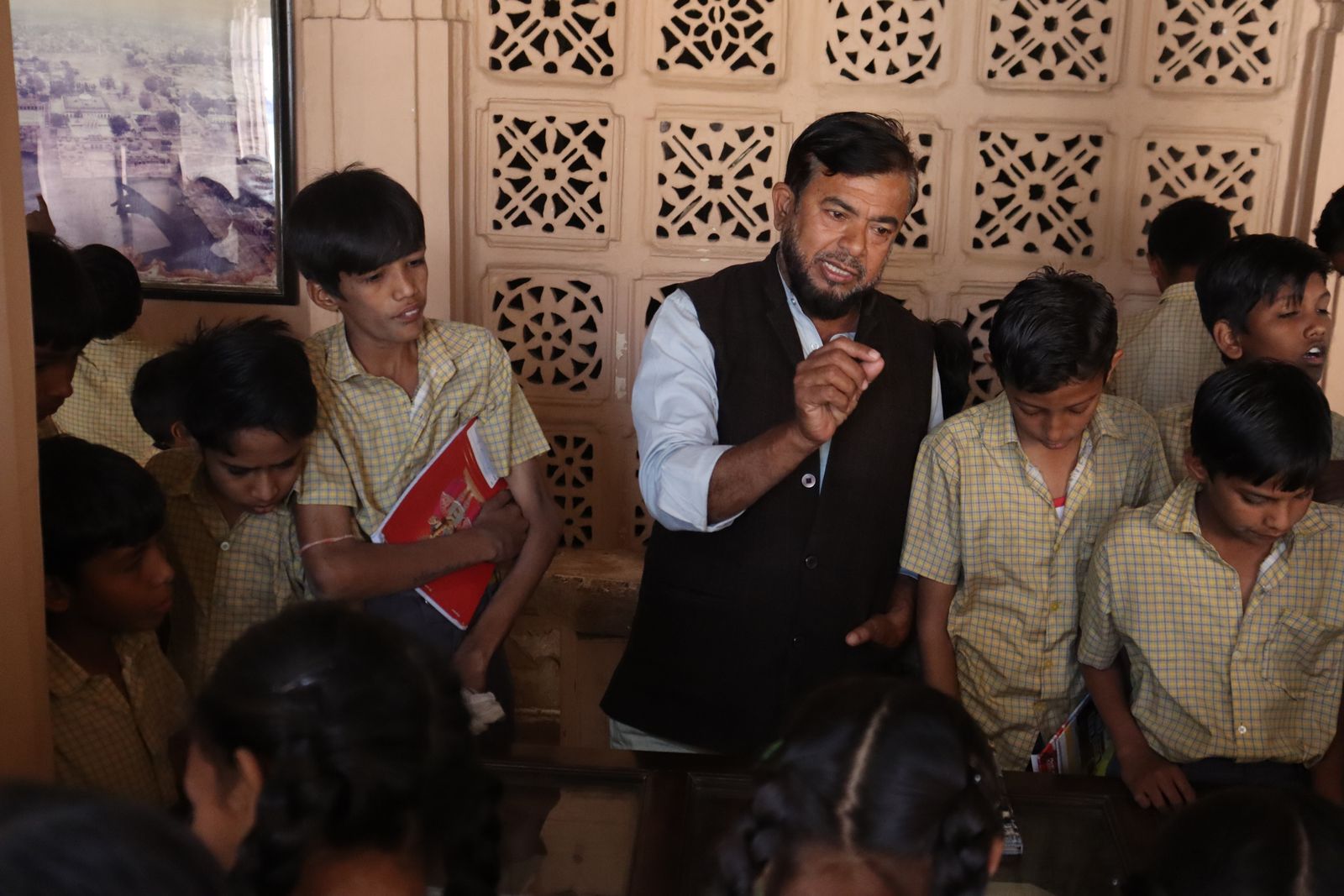 Teacher in a waistcoat explaining something to a group of schoolboys gathered around him