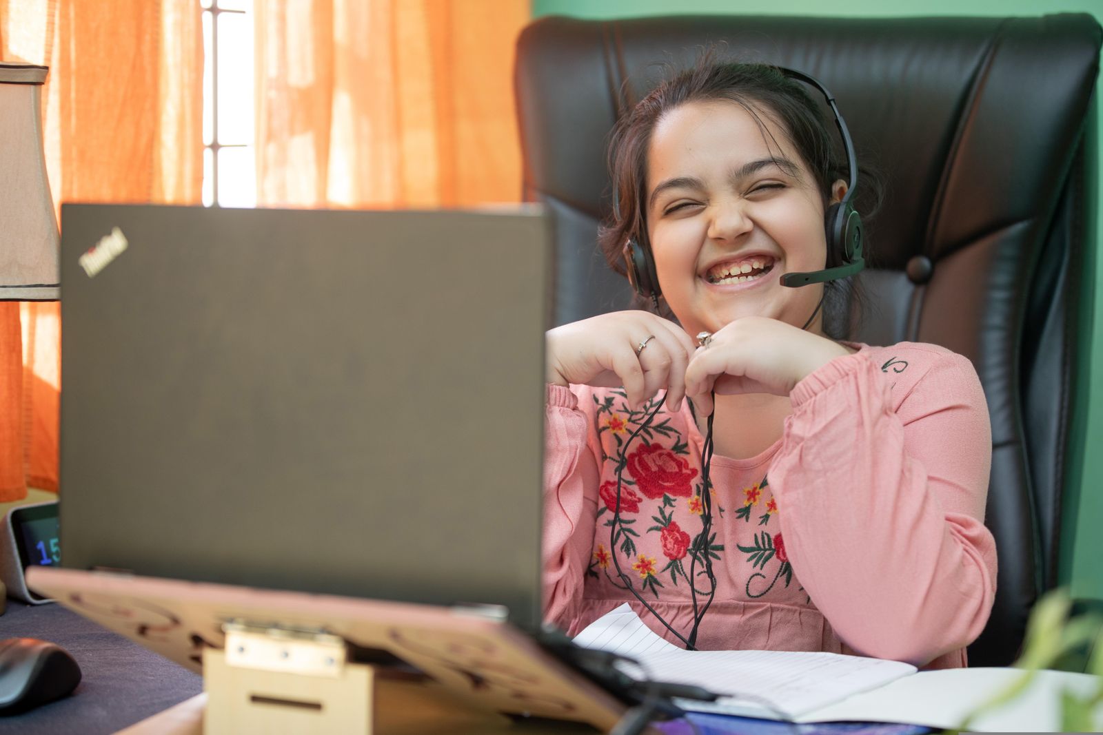 Smiling Indian schoolgirl with a headset studying on a laptop at home