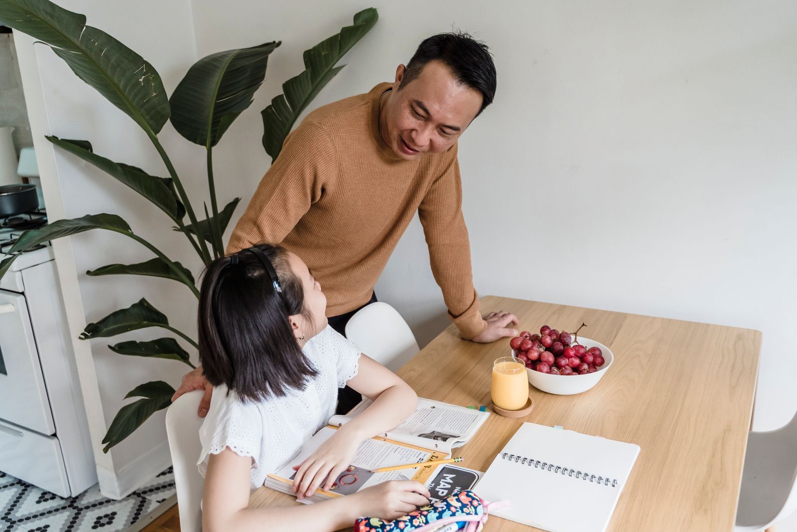 Father sitting with his daughter at the kitchen table as she does homework.