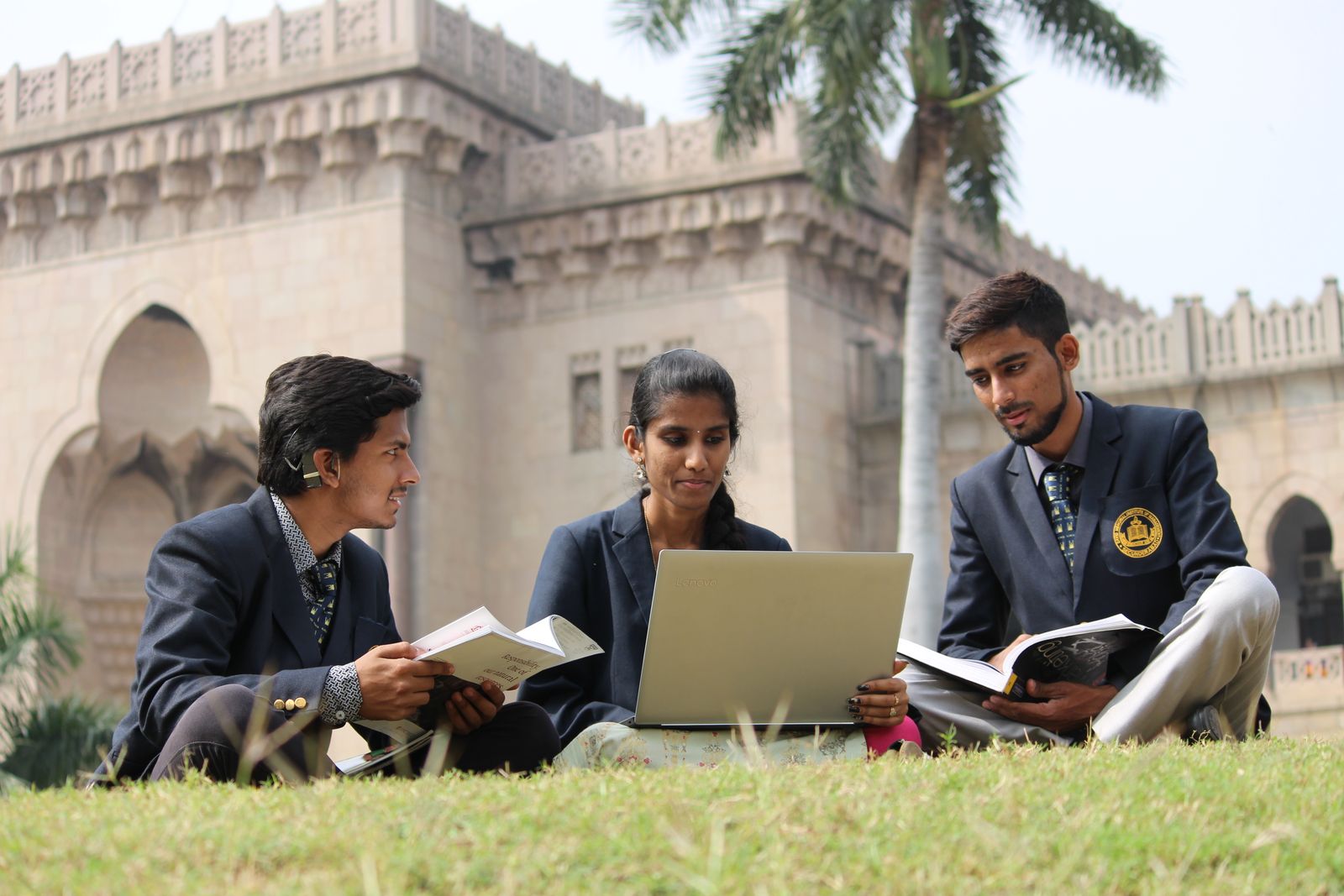 Three students in uniform studying together with books and a laptop.