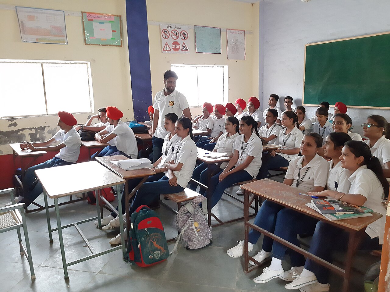 Senior school students in white uniforms sitting at desks in a classroom, listening to a speaker