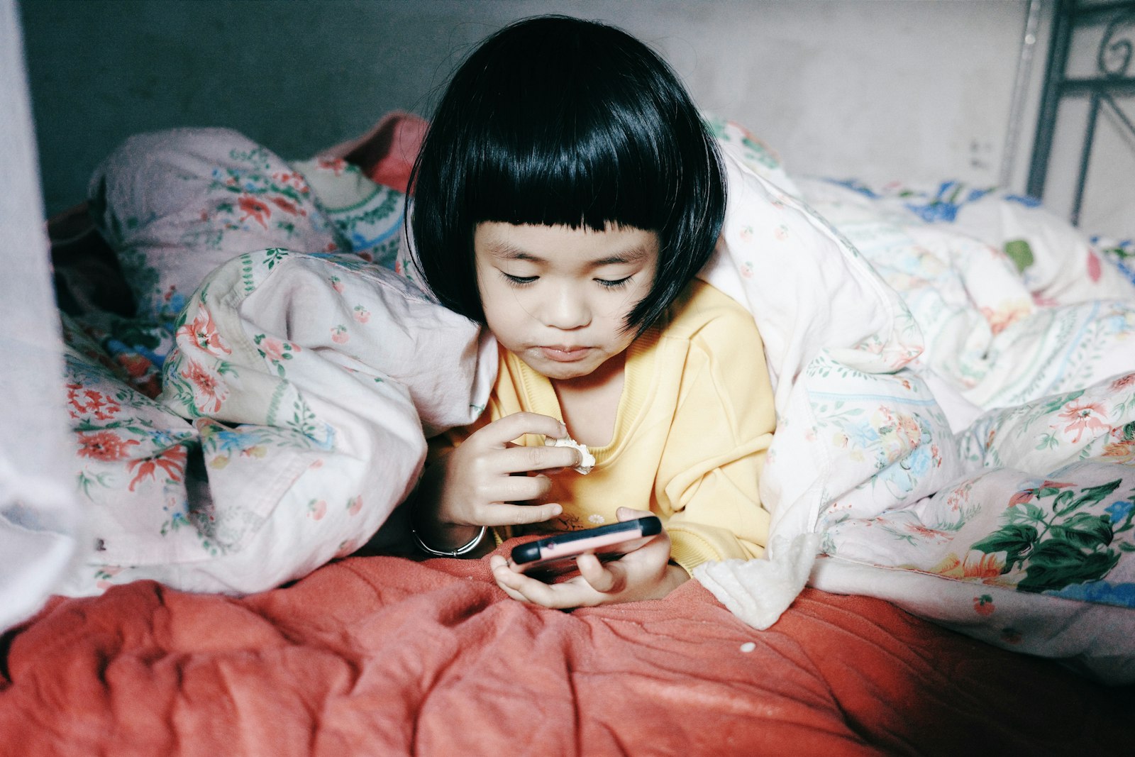 Child lying in bed looking at a phone screen at night