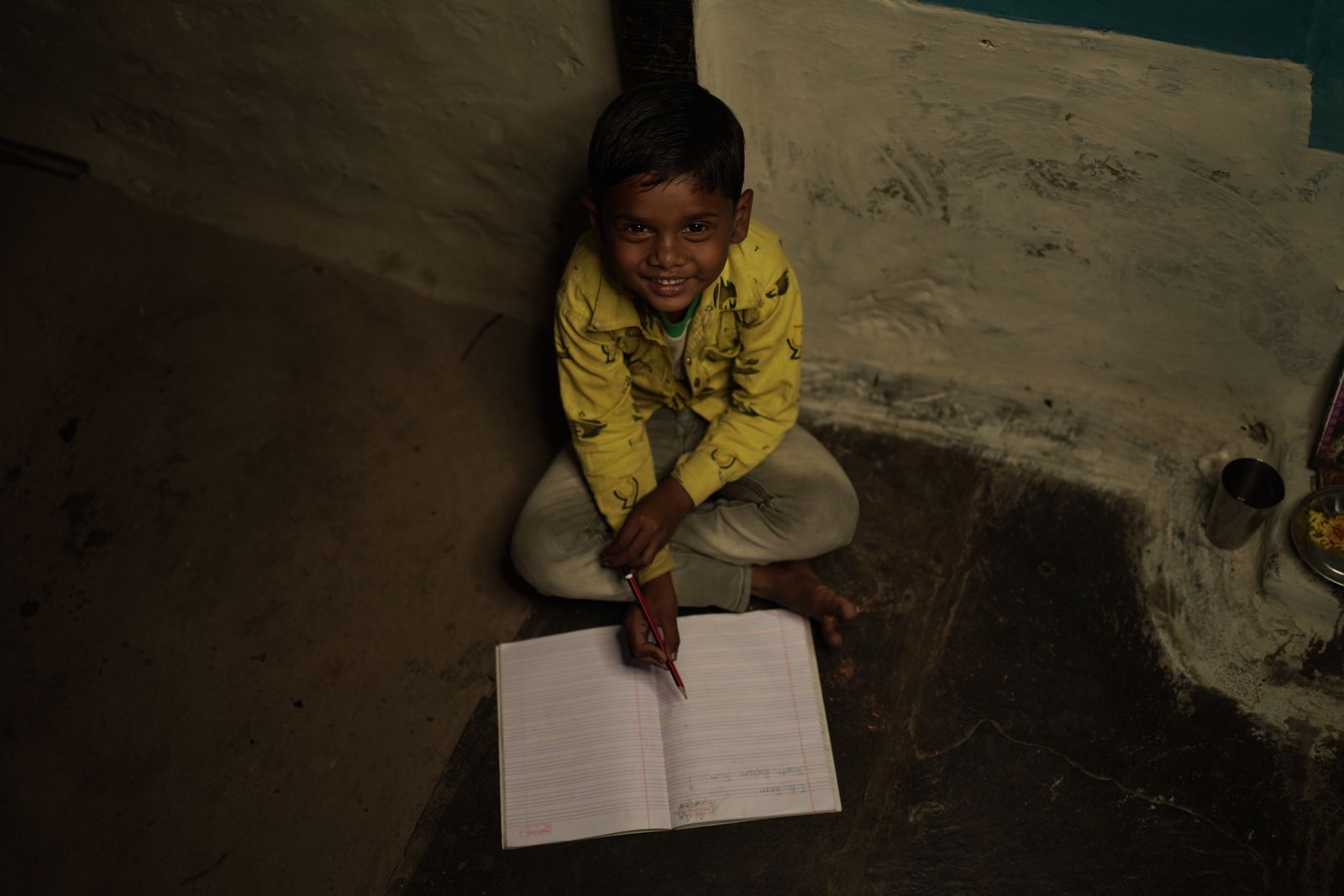 A smiling boy writes in his notebook at home.