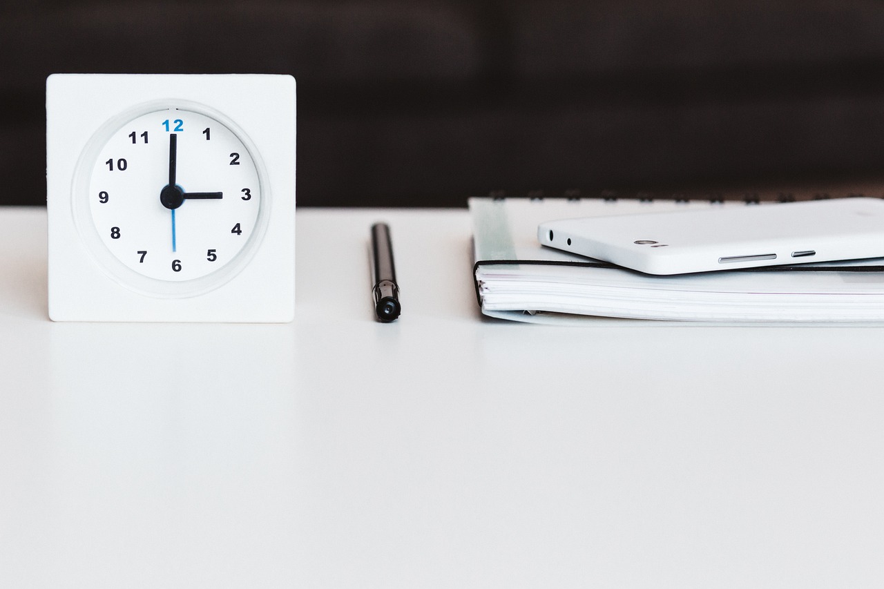 A clock, notebook, pen and phone on a desk, ready for a planned study session.
